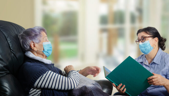 The kind woman talks to her and reads books. Both wear face protective masks and keep their distance due to the coronavirus epidemic.